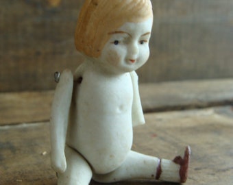 May include: A porcelain doll with a white dress and brown shoes. The doll has a painted face with brown eyes and blonde hair.