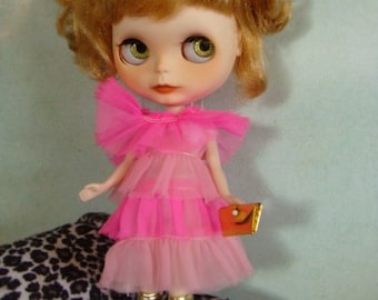 May include: A doll with blonde hair wearing a pink dress, gold shoes, and pink sunglasses. The doll is holding a small orange purse.