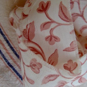 Peut inclure: Gros plan sur un tissu blanc &agrave; motif floral rose. Le tissu est pli&eacute; et pr&eacute;sente une bordure brute.