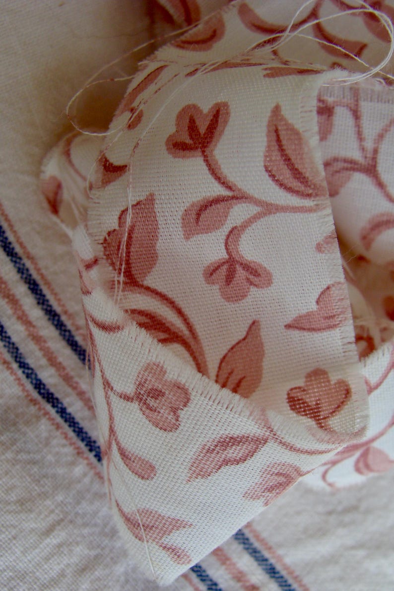 Peut inclure: Gros plan sur un tissu blanc &agrave; motif floral rose. Le tissu est pli&eacute; et pr&eacute;sente une bordure brute.