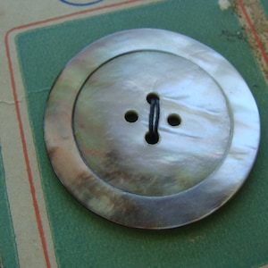 May include: A large, round, iridescent mother-of-pearl button with four holes and a black thread running through it.