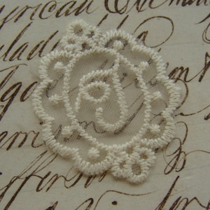 May include: A delicate white lace applique in the shape of a rose. The lace is intricate and detailed, with a floral pattern.