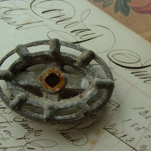 May include: A close-up of a metal knob with a circular design and six spokes. The knob is gray and has a rusty brown center.