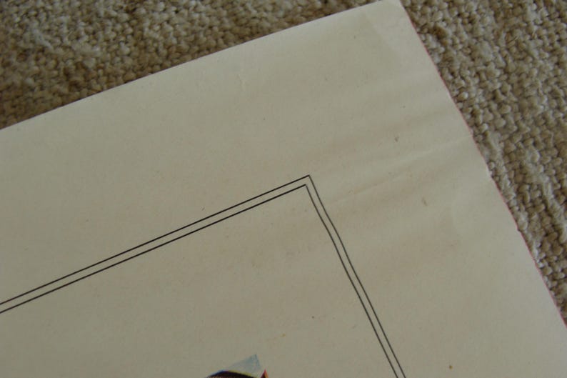 May include: A corner of a cream-colored paper with a double black border. The paper has slight imperfections and is set against a textured, light brown surface.