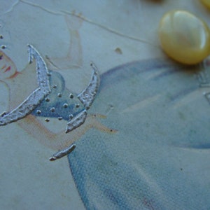 May include: A vintage illustration of a woman in a blue dress with a silver design. The woman is holding a silver design in her hand. The image is on a white background.