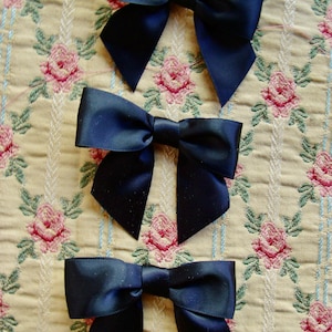 May include: Three black satin bows with a center loop. The bows are arranged vertically on a patterned fabric background.