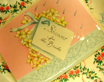 May include: A pink and blue bridal shower invitation with a white tag that says "a shower for the bride". The tag is decorated with a blue ribbon and white flowers.