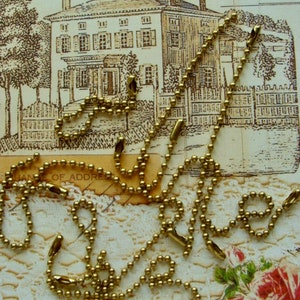 May include: A close-up of a gold chain with round links. The chain is lying on a white lace surface with a floral pattern. The chain is made of metal and has a shiny finish.