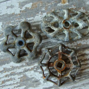 May include: Three vintage metal water valve handles with a rustic, aged finish. The handles are in the shape of a star, a circle, and an oval. They are all rusty and have a worn look.