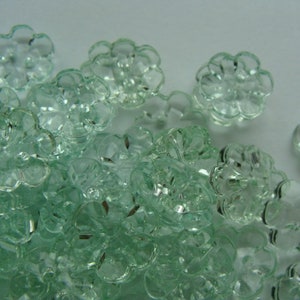 May include: A large group of clear, light green, flower-shaped buttons. The buttons are made of glass and have a slightly frosted finish.