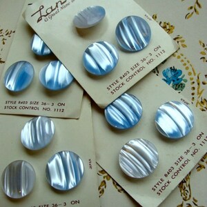 May include: A close-up of a set of six iridescent blue and white buttons with a rippled texture. The buttons are arranged on white cards with the text "Lansing, A Great Name in Buttons" and "STYLE 8403 SIZE 36-3 ON STOCK CONTROL NO. 1112" printed on them.