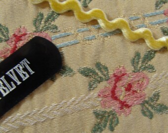 May include: A close-up of a black velvet hair comb with the words "Velvet" printed in white on the comb. The comb is lying on a beige fabric with a floral pattern.