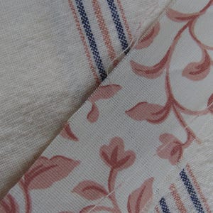 Peut inclure: Deux morceaux de tissu cousus ensemble. Un morceau est blanc avec des rayures roses et bleues. L'autre morceau est blanc avec un motif floral rose.