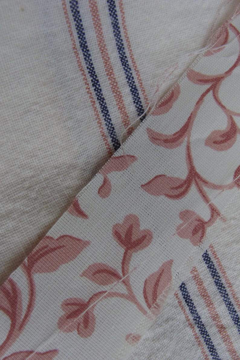 Peut inclure: Deux morceaux de tissu cousus ensemble. Un morceau est blanc avec des rayures roses et bleues. L'autre morceau est blanc avec un motif floral rose.