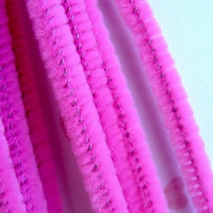 May include: Close-up of several pink pipe cleaners, also known as chenille stems, with a fuzzy texture. The pipe cleaners are arranged vertically and are in focus.