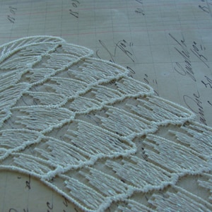 May include: White lace trim with a delicate, scalloped edge. The lace is made of small, white beads that are sewn together in a pattern of overlapping scales.