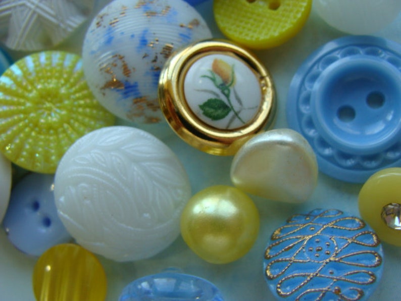 May include: Assortment of colorful buttons in various shapes and sizes, including white, blue, yellow, and floral designs.