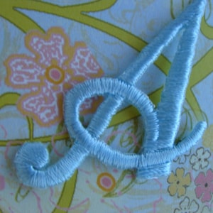 May include: A light blue embroidered letter A, with a floral pattern in the background.