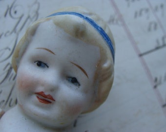May include: A porcelain doll with a blue ribbon in her hair. Her eyes are closed and she has a sweet expression on her face.