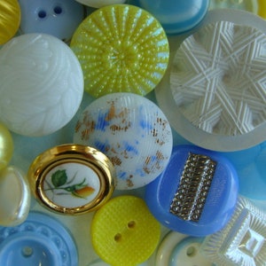May include: Assortment of vintage buttons in various colors and patterns, including yellow, blue, white, and gold. The buttons are made of different materials, such as plastic, metal, and ceramic. Some buttons have intricate designs, while others are simple and plain.