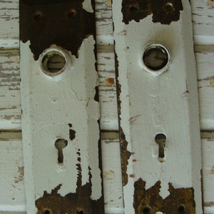 May include: Two antique white door plates with a keyhole and a round hole for a knob. The plates are made of metal and have a distressed finish.