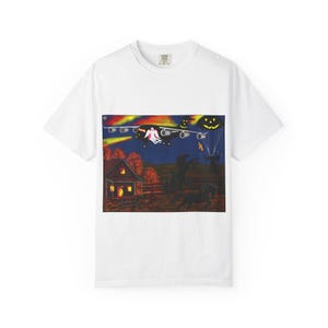 Puede incluir: Una camiseta blanca de manga corta con un estampado gráfico de una escena nocturna oscura con un gran avión de carga, un fantasma, un paracaídas de calabaza, una casa con ventanas iluminadas, dos caballos negros y una figura con antorcha.