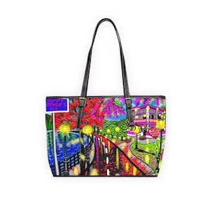 Puede incluir: Bolso tote de cuero negro con una colorida ilustración de una escena callejera. La obra de arte incluye un letrero que dice "Happy Mother's Day". El bolso tiene asas negras y herrajes plateados.