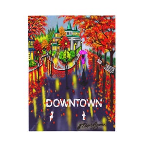 Op de afbeelding: Een schilderij van een straatbeeld in de binnenstad in de herfst. Het kunstwerk toont een persoon met een roze paraplu die op een natte straat loopt, met gebouwen en bomen op de achtergrond. Het woord "DOWNTOWN" wordt in witte tekst weergegeven.