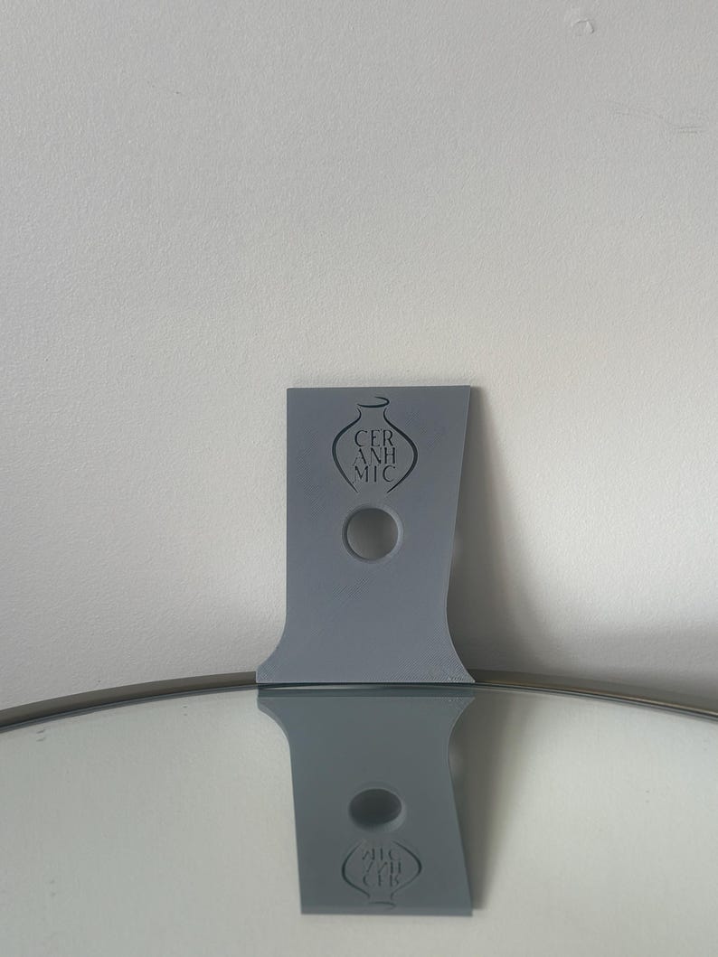 May include: A grey ceramic vase stand with a hole in the centre and the word "CERAMIC" printed on the front.