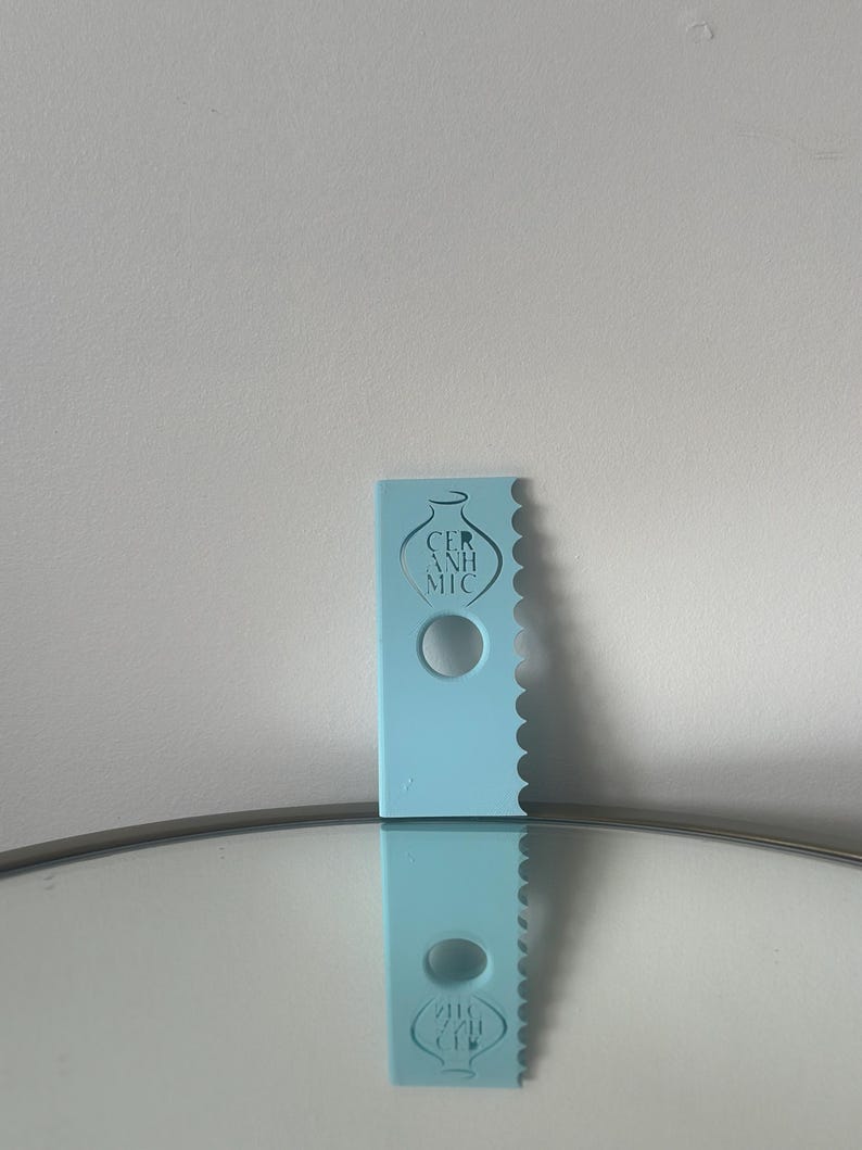 May include: A light blue plastic cake decorating tool with a scalloped edge and a hole in the centre. The tool has the text "CERAMIC" printed on it.