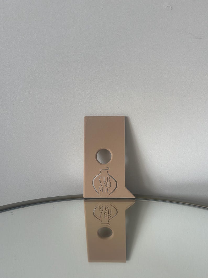 May include: A light brown ceramic bottle stopper with a hole in the top and the words "Ceramic" in a stylised font.