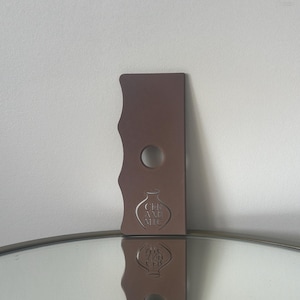 May include: A brown ceramic tool with a wavy edge and a hole in the centre. The tool has the words "Ceramic Art Nic" engraved on it.