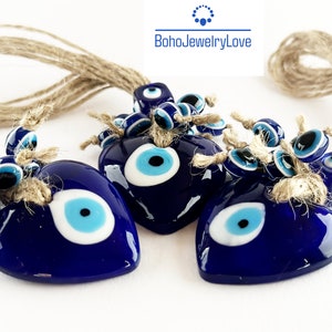 May include: Three blue glass heart-shaped evil eye charms with smaller evil eye beads hanging from them. The charms are strung on a natural jute twine.