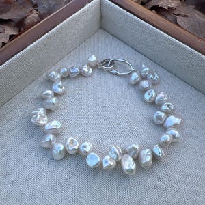 May include: A white pearl necklace with a silver clasp. The pearls are irregular in shape and have a natural, organic look.