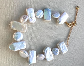 May include: A white pearl necklace with an adjustable gold chain closure. The pearls are irregular in shape and size, with some being rectangular and others being round.