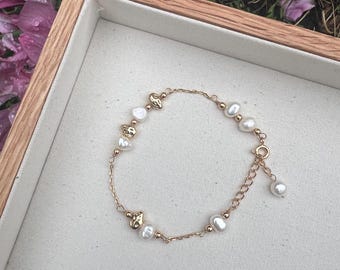 May include: A delicate gold chain bracelet with irregular white pearls and gold accents. The bracelet is displayed in a wooden box.