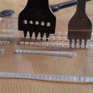 May include: Leatherworking tools including a black leather punch and a silver leather punch are displayed on a clear acrylic guide with measurements in millimeters. The guide is labeled with "R9" and measurements from 3 mm to 6 mm. A coin is also visible.