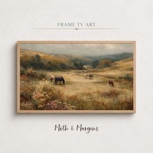 May include: A landscape painting in a light wood frame titled FRAME TV ART. The artwork depicts a wide, grassy field with several horses grazing under a cloudy, overcast sky. The scene features muted tones of brown, gold, and green, with rolling hills in the distance and wildflowers in the foreground. The text MOTH & MARGINS is printed below the frame.