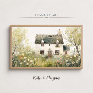 Può includere: Dipinto ad acquerello di un cottage bianco con tetto grigio, circondato da un giardino di fiori rosa e bianchi. L'opera è incorniciata in una cornice di legno chiaro. Il testo "FRAME TV ART" è in alto e "Moth & Margins" in basso.