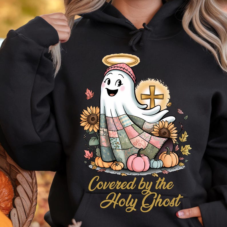 K&ouml;nnte beinhalten: Schwarzer Kapuzenpullover mit einem Cartoon-Geist mit Heiligenschein und einem Patchwork-Design. Der Geist ist von Sonnenblumen, K&uuml;rbissen und Herbstbl&auml;ttern umgeben. Der Text "Covered by the Holy Ghost" ist unten aufgedruckt.