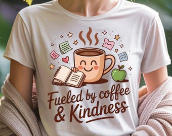 Puede incluir: Camiseta blanca con un dibujo animado de una taza de café sonriente, un libro abierto y una manzana verde. El texto "Fueled by coffee & Kindness" está debajo. La camiseta tiene mangas cortas.