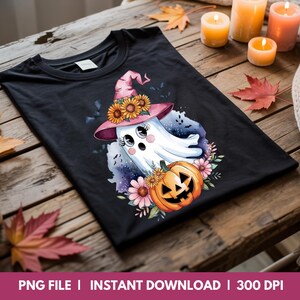 May include: Black t-shirt with a Halloween-themed design. It features a cartoon ghost in a pink witch hat decorated with sunflowers, a carved pumpkin, and flowers. The design also includes bats and floral elements.