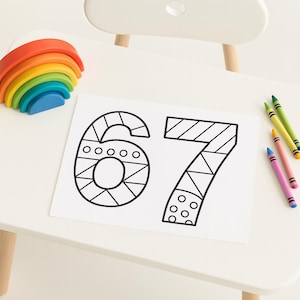 May include: A white sheet of paper with the numbers 67 outlined in black, ready to be colored. A rainbow-colored wooden arch and several crayons in various colors are also present.