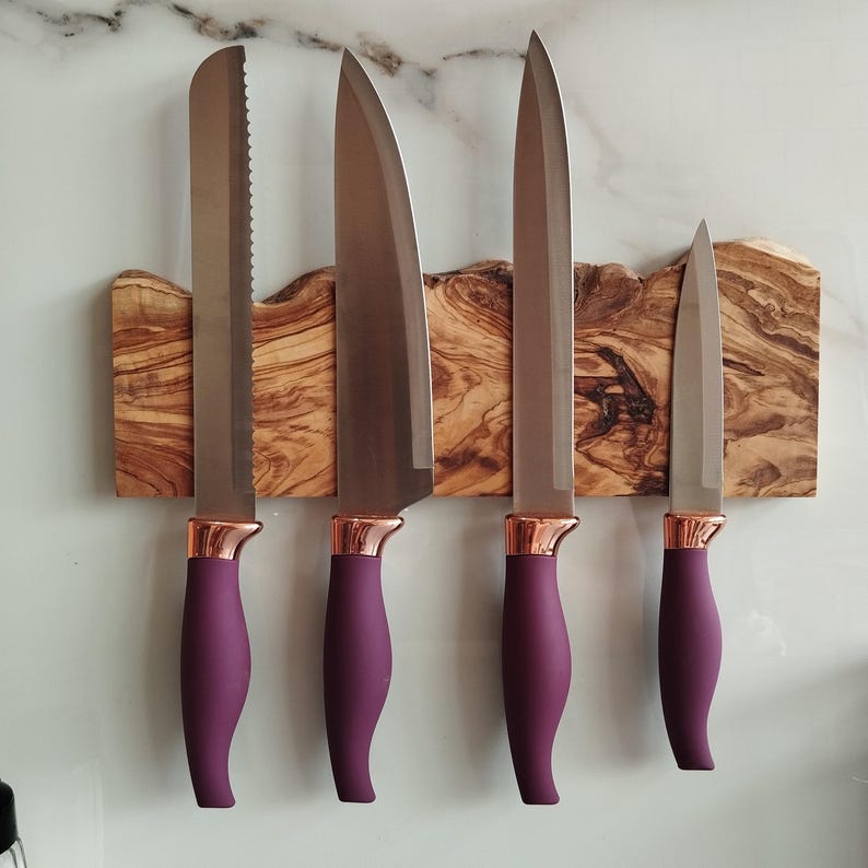 Pu&ograve; includere: Quattro coltelli da cucina con manici viola e dettagli in oro rosa sono montati su un portacoltelli magnetico in legno. Il supporto &egrave; in legno di ulivo con venature del legno naturali.