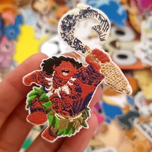 Puede incluir: Parche bordado con un personaje de dibujos animados con piel roja, una falda de hierba y un gran gancho. El parche tiene un borde blanco y está rodeado de otros parches coloridos. El gancho es beige y azul.