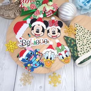 May include: A collection of Christmas-themed Disney character patches and decorations. Mickey and Minnie Mouse, Stitch, Donald Duck, and Daisy Duck are shown wearing Santa hats. The word "Believe" is spelled out in decorative letters, with a green and red bow.
