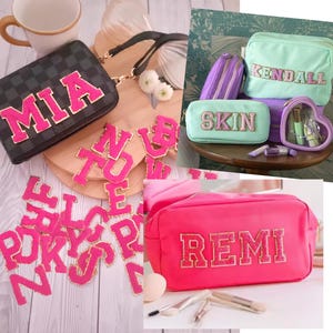 Pode incluir: Uma coleção de nécessaires personalizadas de cor rosa e branca com os nomes Mia, Kendall, Skin e Remi. Os nécessaires são feitos de um material macio de tecido e têm um fecho de correr.