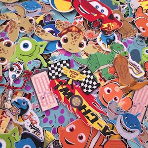 May include: A collection of embroidered fabric patches featuring various animated characters and symbols, including a red race car, a green dinosaur, a clownfish, a blue fish, a green one-eyed monster, a white spork character, and a cowboy boot.