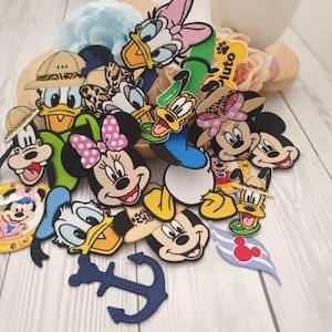May include: A collection of embroidered fabric patches featuring various Disney characters including Mickey Mouse, Minnie Mouse, Donald Duck, Daisy Duck, Goofy, and Pluto, along with a dark blue anchor shape and a light blue striped wing emblem.