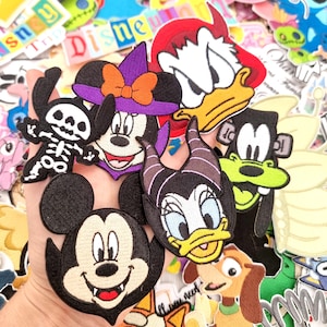 May include: A selection of colourful embroidered patches featuring Disney characters. Patches include Mickey Mouse, Minnie Mouse in a witch hat, Donald Duck, Daisy Duck, Goofy, and a skeleton. Other patches with the word "Disney" are also visible.